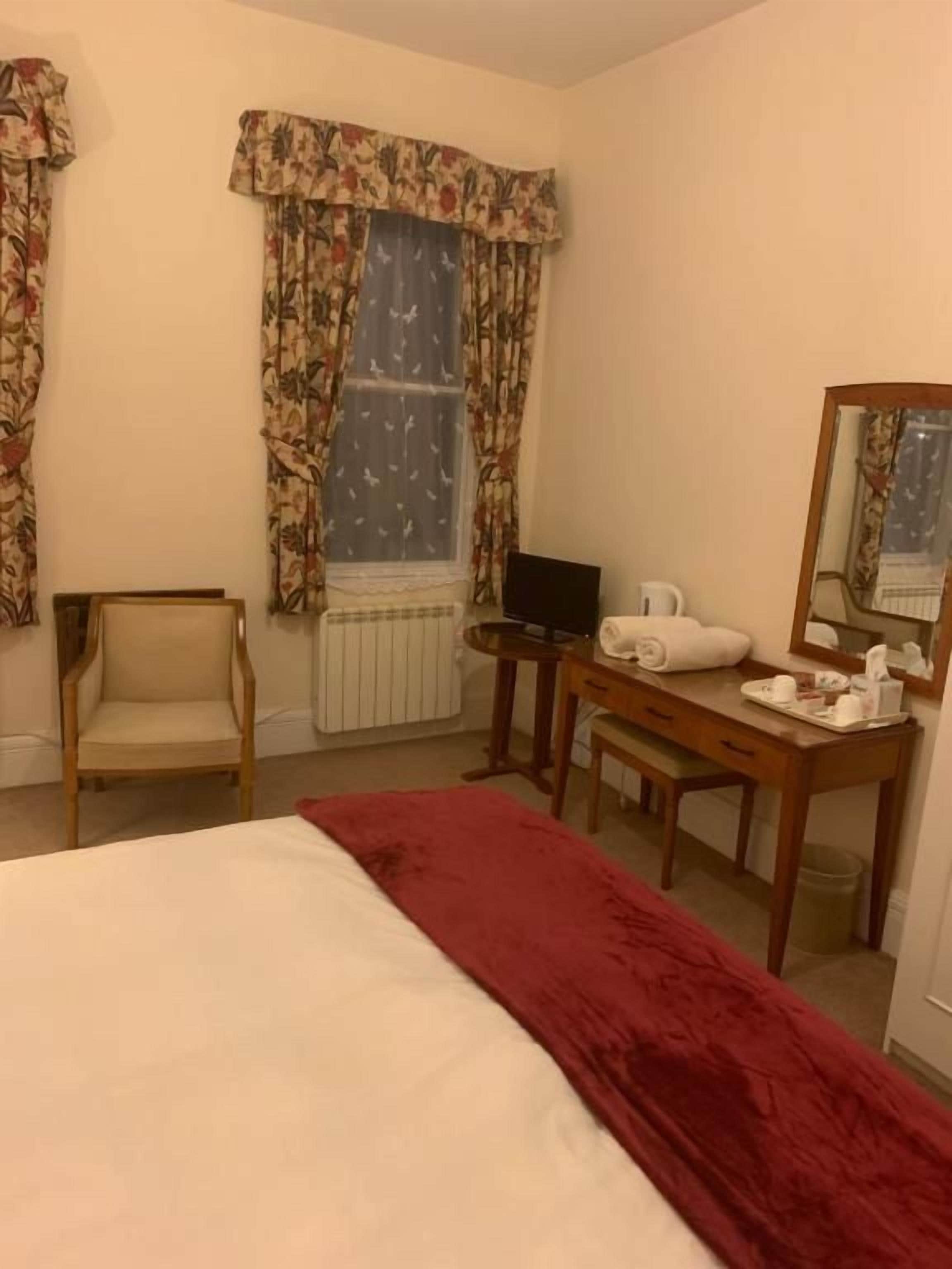 A hotel room with a bed, a desk with a computer, a chair, a mirror, and curtains.