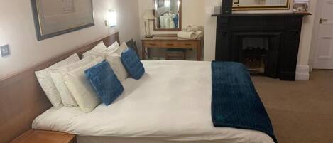 Habitación de hotel con cama, mesita de noche, cómoda, espejo, chimenea y cuadros en la pared.