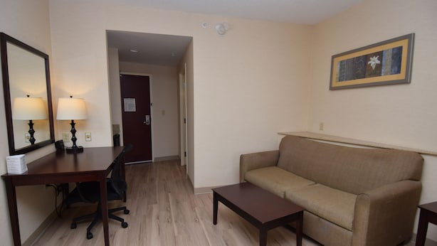 Una habitación de hotel con un escritorio de madera, un sofá color crema, una pequeña mesa de centro y un cuadro en la pared.
