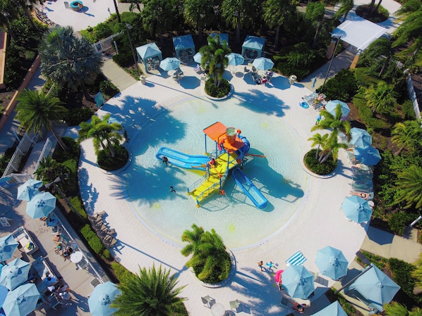 Een waterpark met een centraal speelgebied, omringd door ligbedden en parasols.