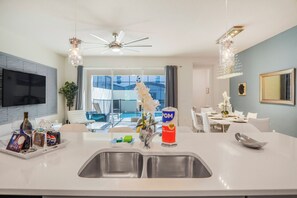 A modern kitchen with a central island, a dining area with a table and chairs, a ceiling fan, and a view of a swimming pool. - Family 5BR at Solara with Private Pool (Kissimmee)