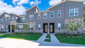 A modern multi-story residential building with a stone facade and multiple windows. - Family 5BR at Solara with Private Pool (Kissimmee)