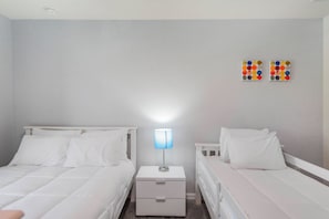 A bedroom with two beds, a nightstand with a lamp, and a wall decoration. - Family 5BR at Solara with Private Pool (Kissimmee)