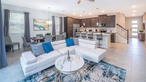 A modern living room with a white sectional sofa, a marble coffee table, and a dining area with a table and chairs. - Family 5BR at Solara with Private Pool (Kissimmee)