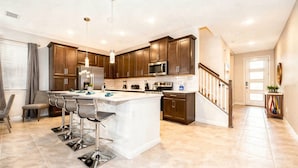 A modern kitchen with a central island, bar stools, stainless steel appliances, and a staircase leading to another level. - Family 5BR at Solara with Private Pool (Kissimmee)