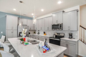 A modern kitchen with white cabinetry, stainless steel appliances, and a central island with a sink and countertop. - Family 5BR at Solara with Private Pool (Kissimmee)