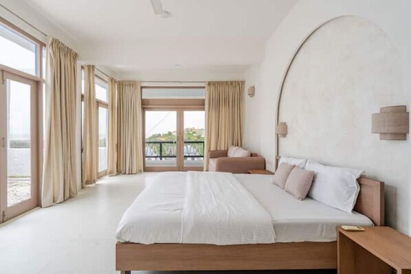A bedroom with a large bed, a nightstand, a sofa, and a view of the outdoors through a glass door.