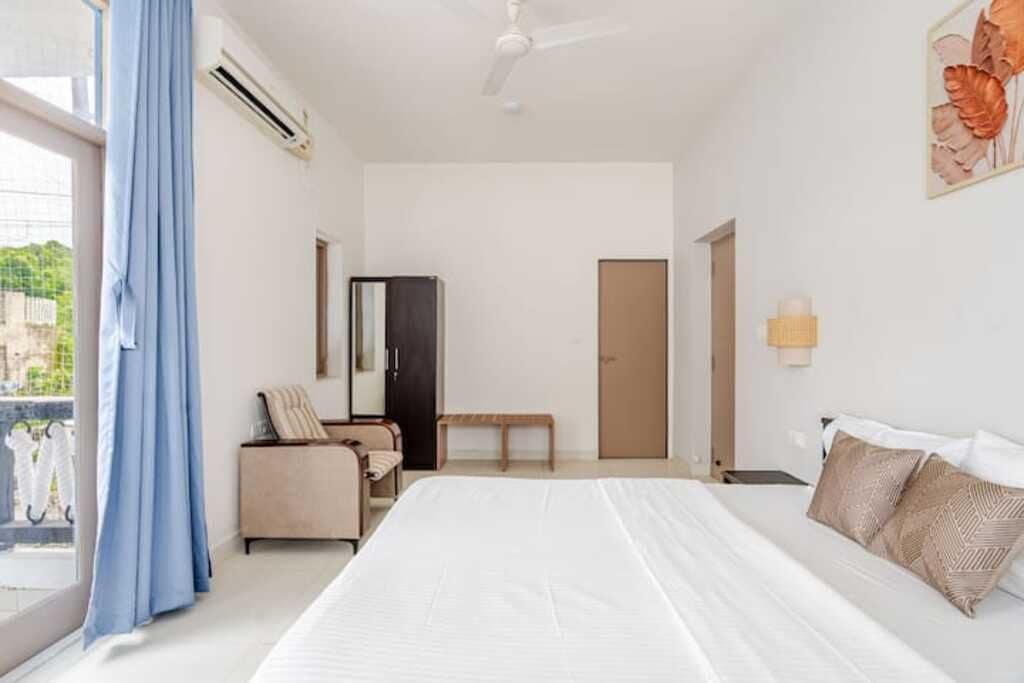 Una habitación de hotel con cama, escritorio, silla, armario y ventana con cortinas.
