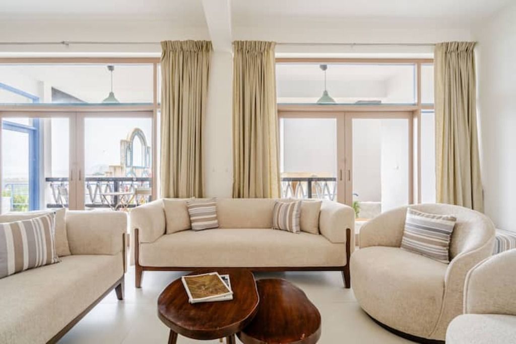 Ein stilvolles Wohnzimmer mit einer Sofagarnitur, einem Couchtisch und großen Fenstern mit Vorhängen.