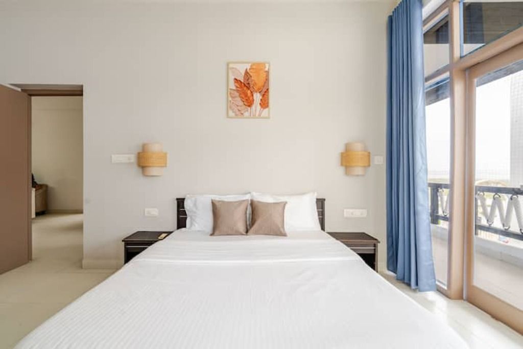 Ein Hotelzimmer mit einem großen Bett, zwei Nachttischen, einem an der Wand hängenden Kunstwerk und Blick durch ein mit Vorhängen drapiertes Fenster.