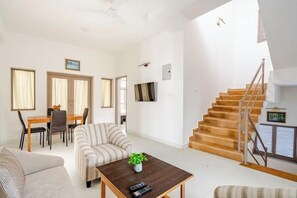 A spacious living area with a sofa, a coffee table with a plant, a dining table with chairs, and a staircase.