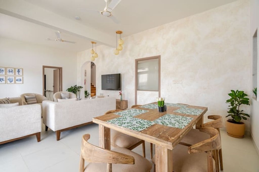 Ein modernes Wohnzimmer mit einem Holzesstisch, beigefarbenen Sofas und einem Deckenventilator.
