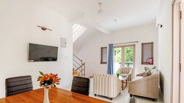 Un coin repas avec une table en bois, des chaises, un vase de fleurs et un téléviseur fixé au mur.