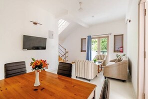 A dining area with a wooden table, chairs, a vase with flowers, and a television mounted on the wall.