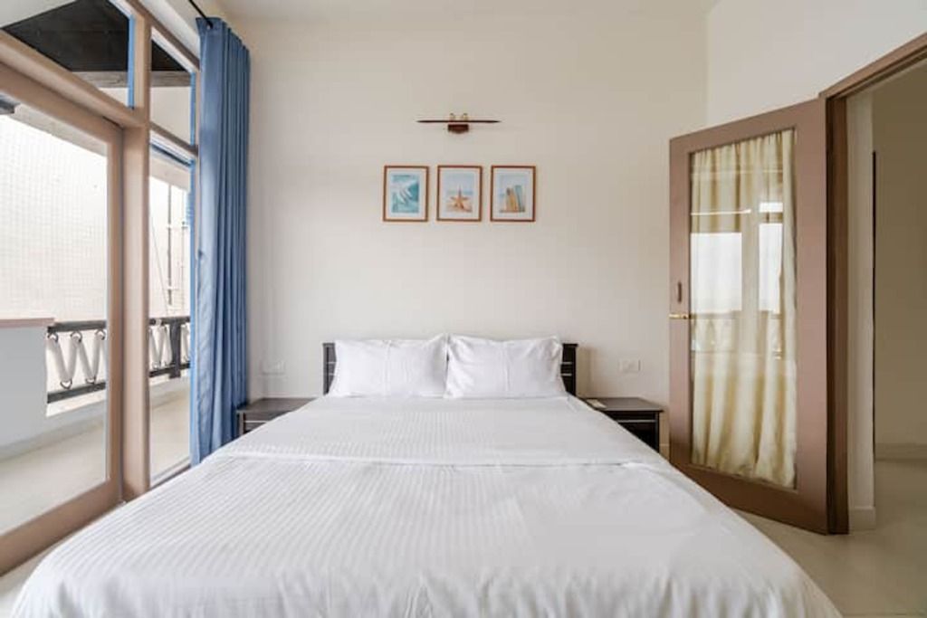 Ein Hotelzimmer mit einem großen Bett, einem Nachttisch, einer Wanduhr und einem Fenster mit Vorhängen.