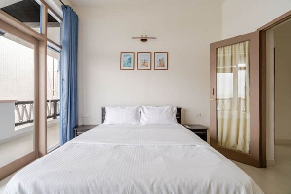 A hotel room with a large bed, a nightstand, a wall-mounted clock, and a window with curtains.