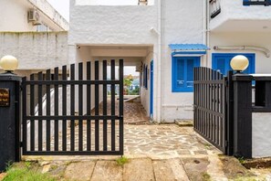 A narrow alleyway with a black gate, white buildings, and blue shutters.