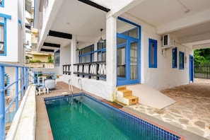 Una piscina con borde de azulejos, una zona cubierta con un banco y una escalera que lleva a una puerta.
