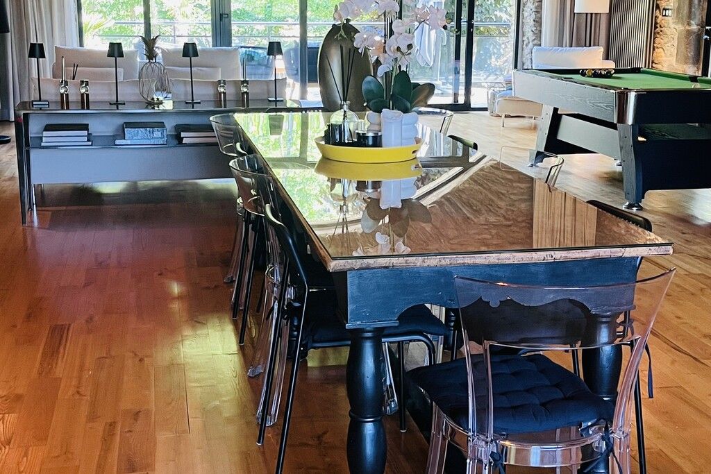 A modern dining area with a wooden table, clear chairs, and a pool table.
