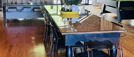 A modern dining area with a wooden table, clear chairs, and a pool table.