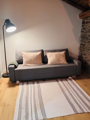 A grey sofa with two cushions, a floor lamp, and a striped rug on a wooden floor. - Renovated Cévennes-style house – heated pool in the forest (Les Plantiers)