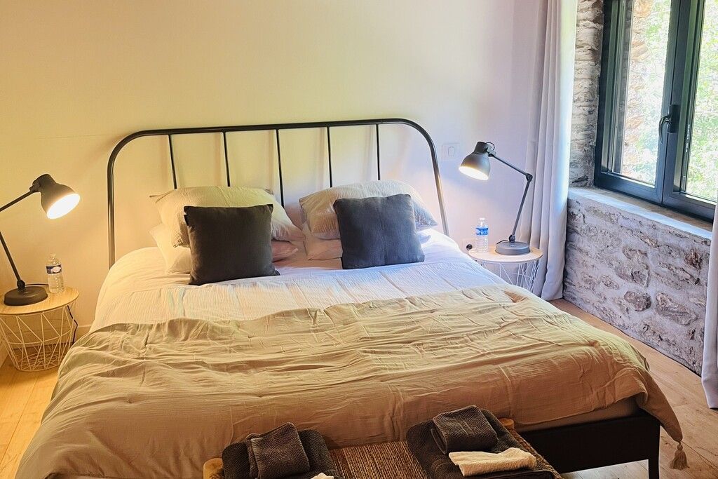 Una cama bien hecha con almohadas, dos lámparas de noche, una botella de agua y una mesita con lámpara.