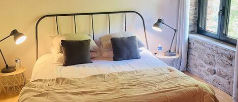 A neatly made bed with pillows, two bedside lamps, a water bottle, and a small table with a lamp.