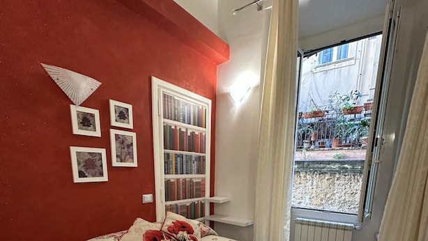 A bedroom with a bed, a bookshelf, and a window with a view of the outside.