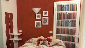 A bedroom with a red accent wall, a bookshelf, and a bed with floral bedding.