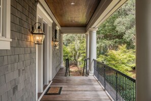 A covered porch with a wooden floor, white columns, and black railings. - 61 River Marsh Lane, Kiawah Island (Kiawah Island)
