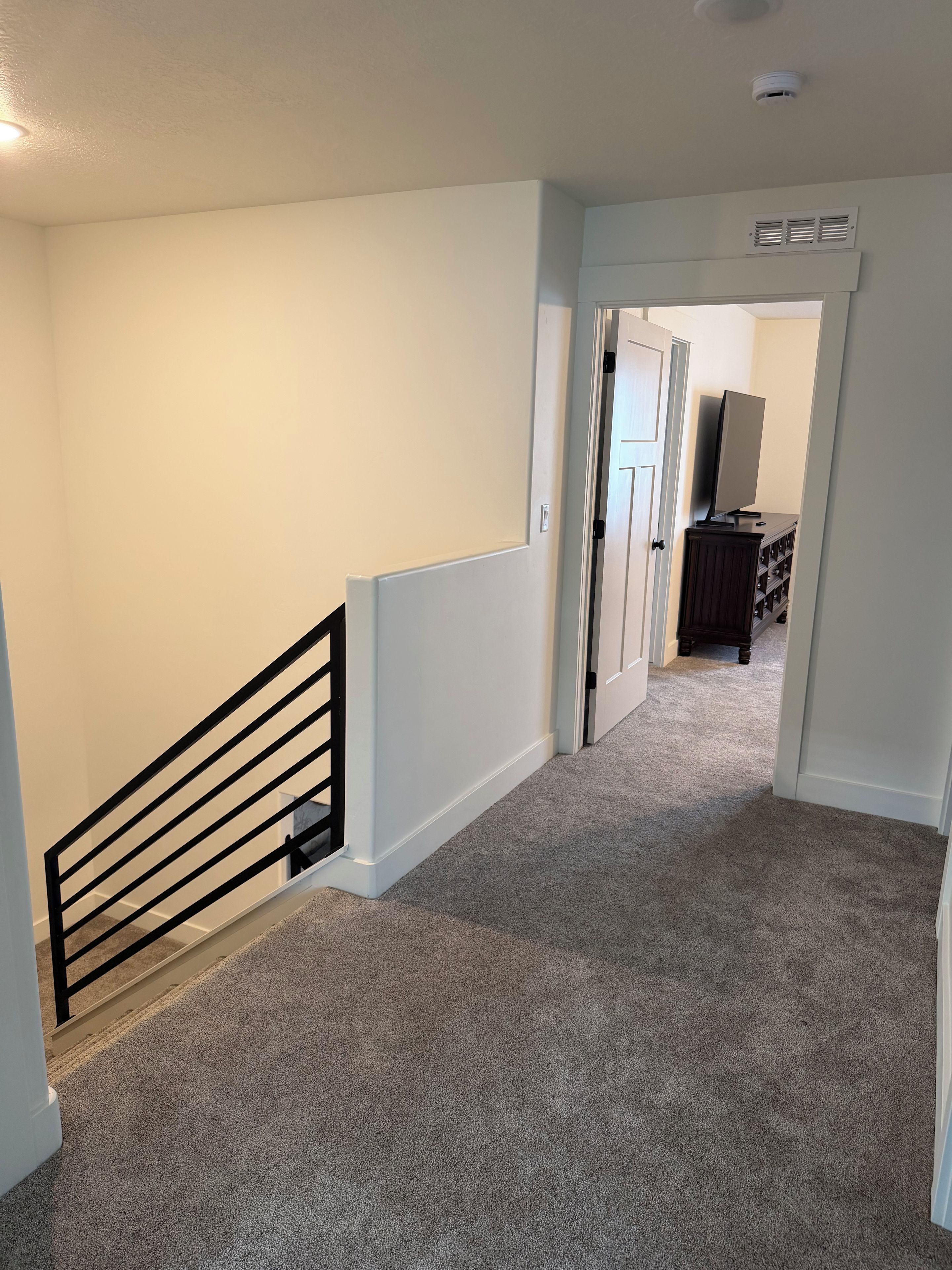 A carpeted hallway with a black railing, white walls, and a door leading to another room.