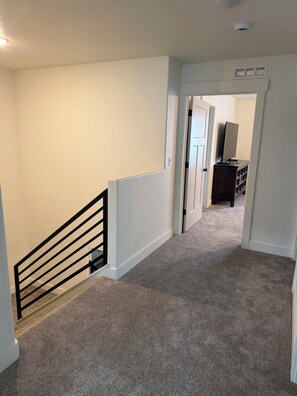 A carpeted hallway with a black railing, white walls, and a door leading to another room.