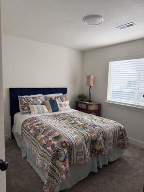 A bedroom with a bed, a nightstand, a lamp, and a window with blinds.