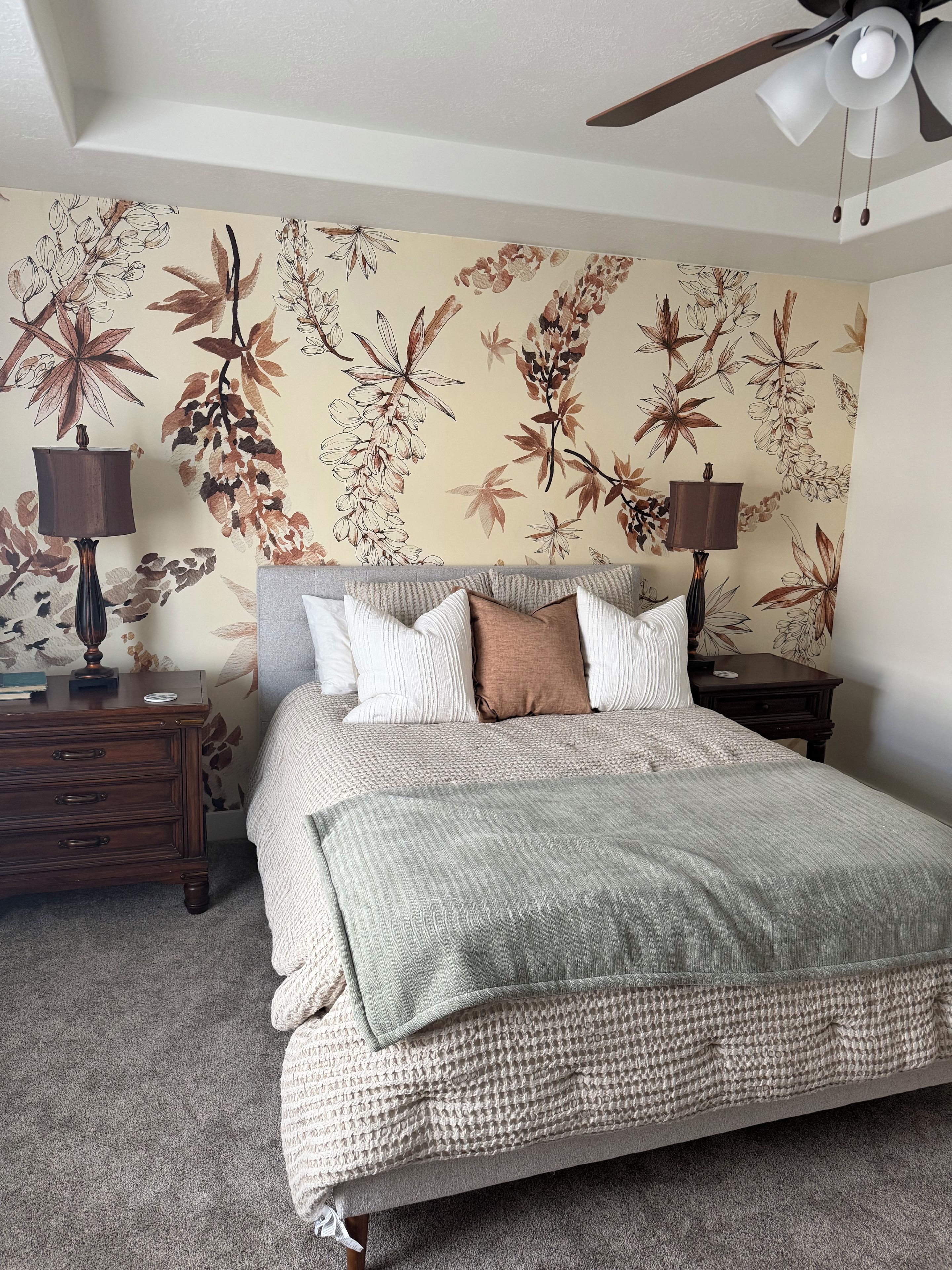 Een slaapkamer met een bed, twee nachtkastjes, een plafondventilator en bloemenbehang.