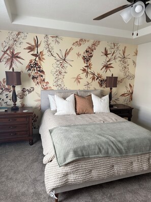 A bedroom with a bed, two nightstands, a ceiling fan, and a floral wallpaper.