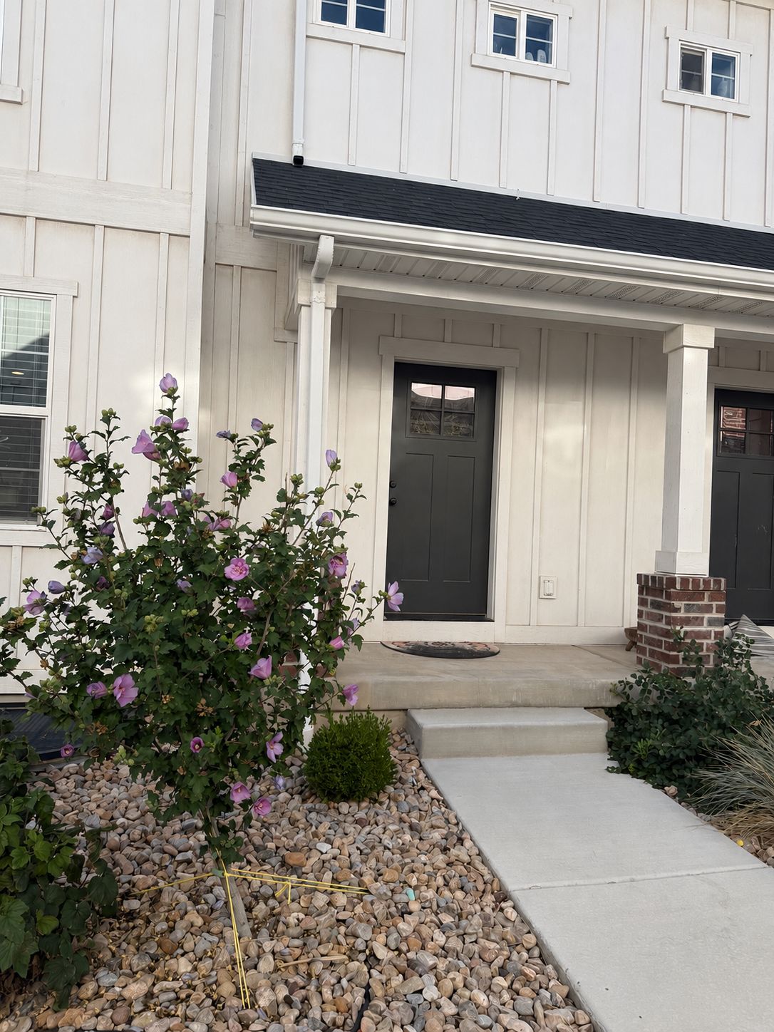 A two-story building with a front porch, a black door, and a small brick structure to the right.