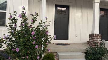 A two-story building with a front porch, a black door, and a small brick structure to the right.