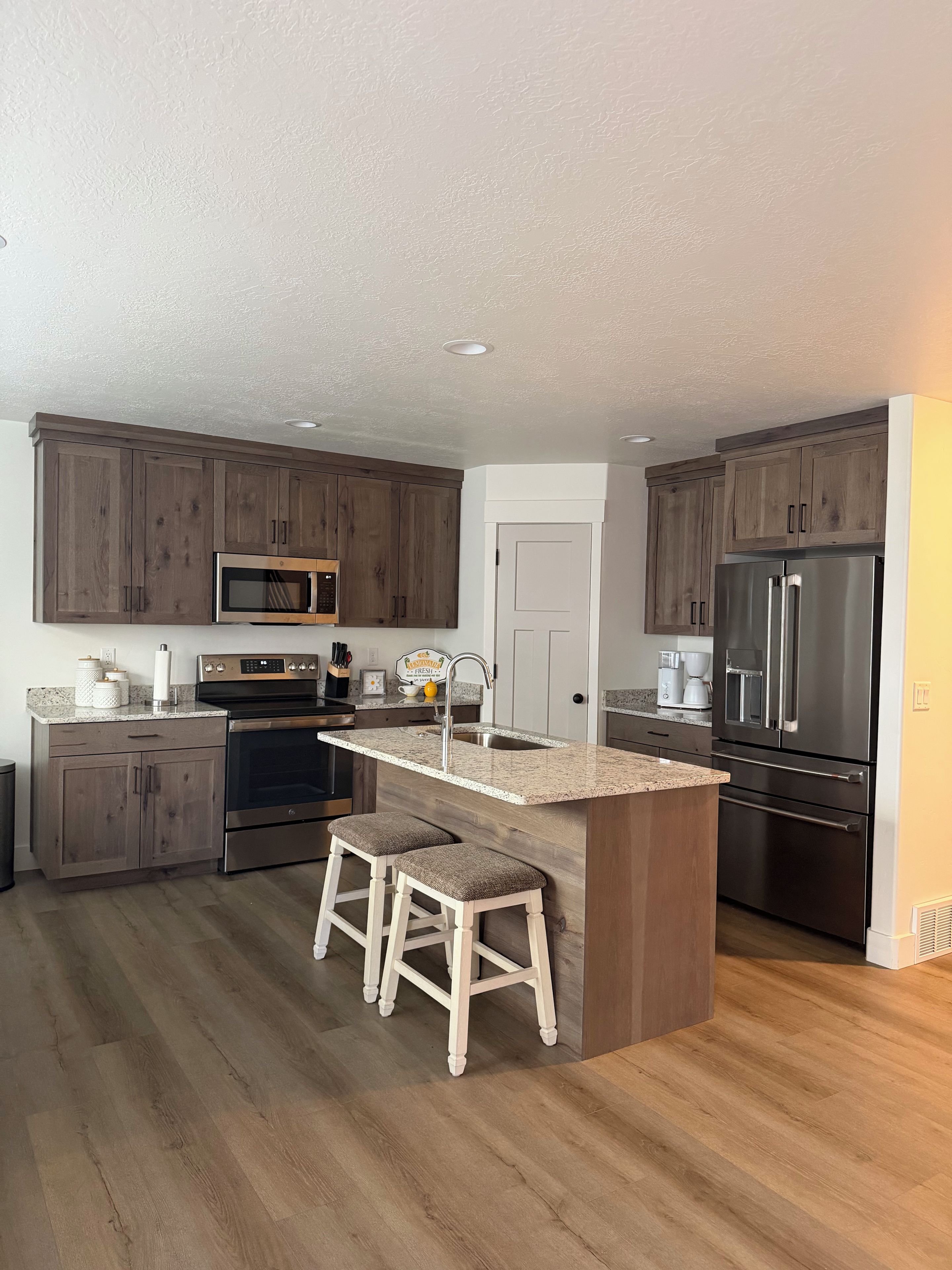 A kitchen with wooden cabinets, stainless steel appliances, a granite countertop, and a central island with stools.
