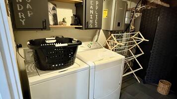 A laundry room with a washing machine, a dryer, a shelf with a cactus, and a sign indicating 'SOAP SUPPLIES CLEANING'.
