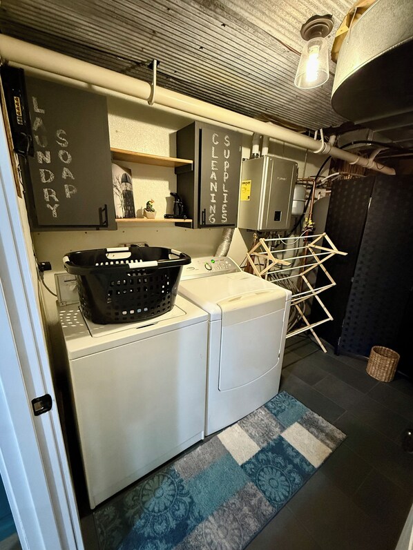 A laundry room with a washing machine, a dryer, a shelf with a cactus, and a sign indicating 'SOAP SUPPLIES CLEANING'.