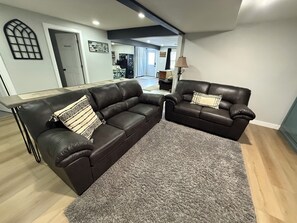 A living room with two leather sofas, a grey rug, and a dining area in the background.
