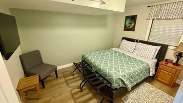 A bedroom with a bed, a chair, a nightstand, a wall clock, a picture, and a window with blinds.