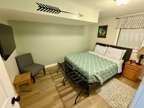A bedroom with a bed, a chair, a nightstand, a wall clock, a picture, and a window with blinds.
