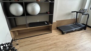 Kuntosali, jossa on juoksumatto, jumppapalloja ja seinään asennettu ilmastointilaite.