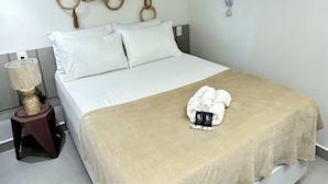 Hotellihuone, jossa on sänky, yöpöytä lampun kanssa ja seinäkoriste.