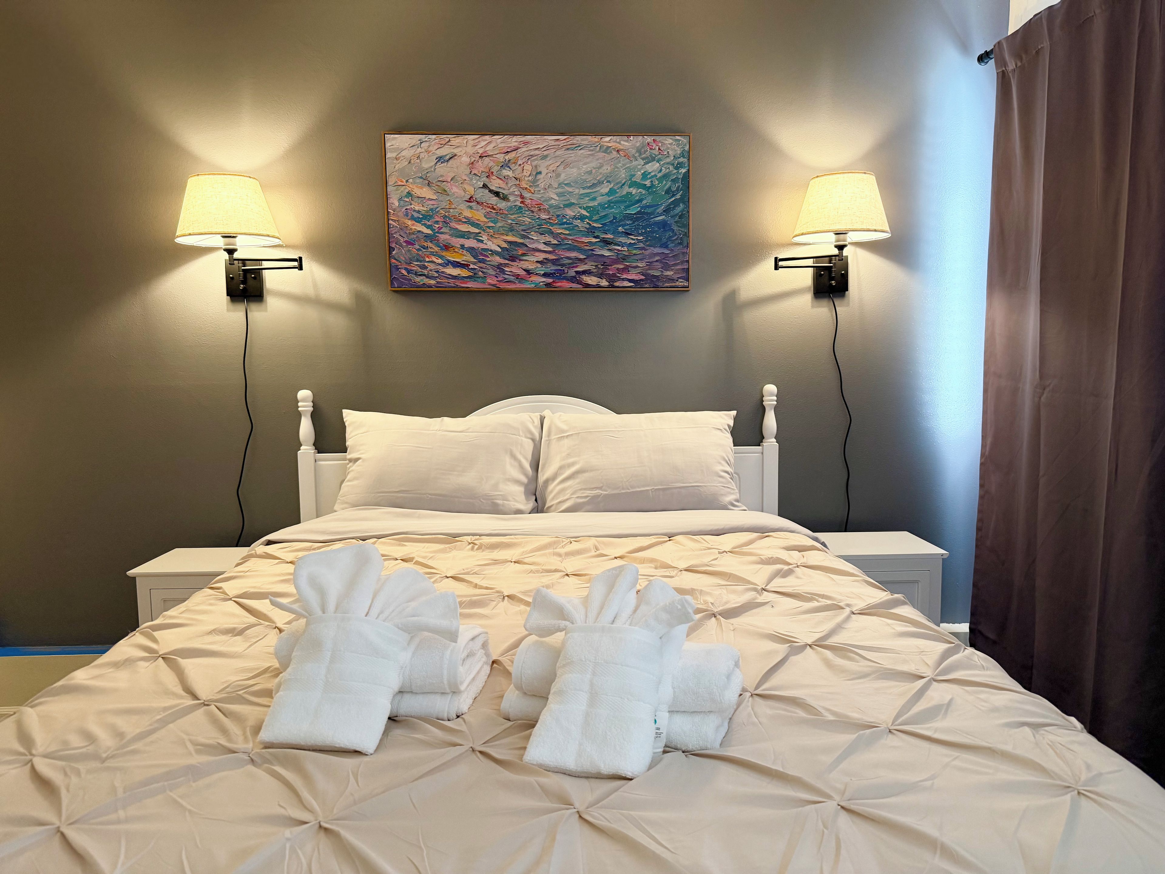A hotel room with a bed, two bedside lamps, a painting on the wall, and towels on the bed.
