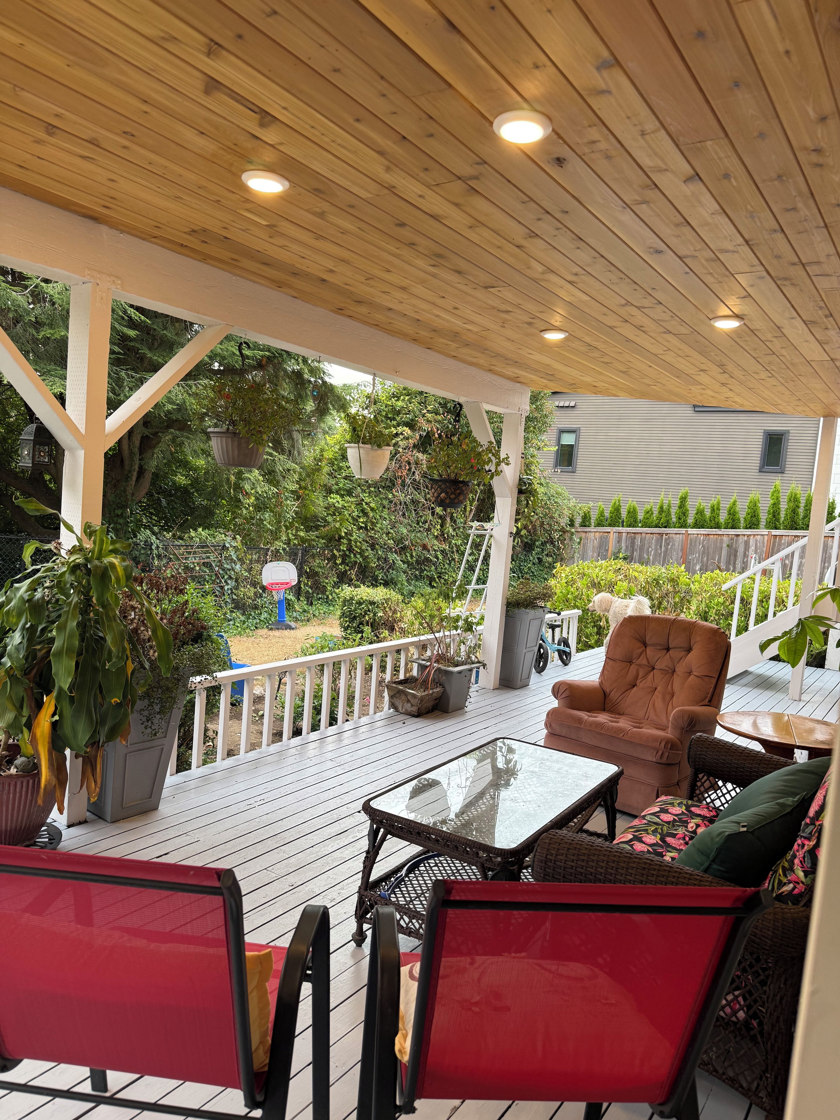 A covered outdoor patio with a wooden ceiling, a white railing, and a seating area with a table and chairs.
