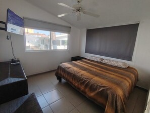Een slaapkamer met een bed, een bureau, een stoel, een plafondventilator en een raam.