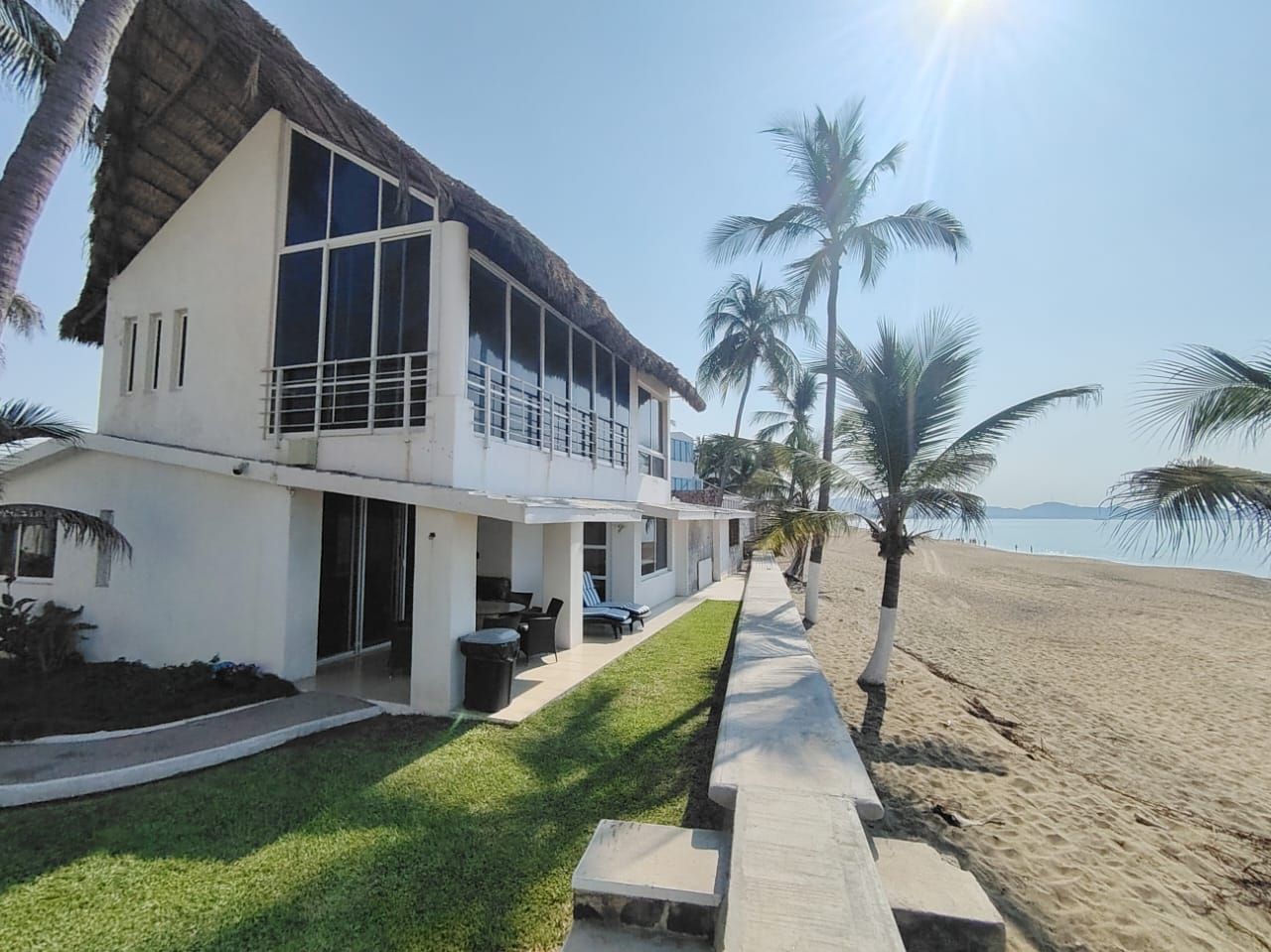 A modern two-story house with a balcony, a lawn, and a pathway leading to a beach.