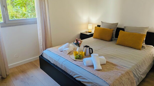 Habitación de hotel con cama, mesitas de noche, ventana con cortinas y vistas a zonas verdes.